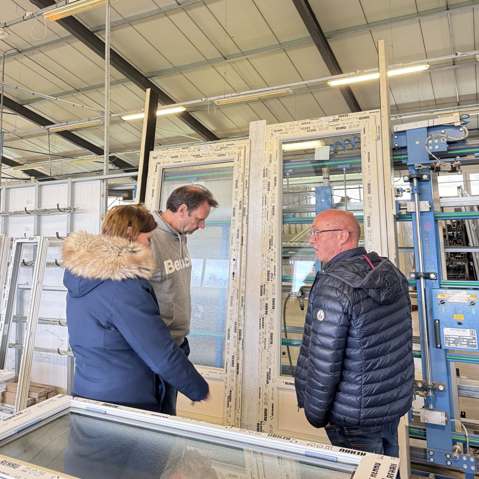 Trois personnes examinant une fenêtre en cours de fabrication dans l'atelier de production de PVC 46, illustrant le contrôle qualité et l'expertise artisanale de l'équipe.